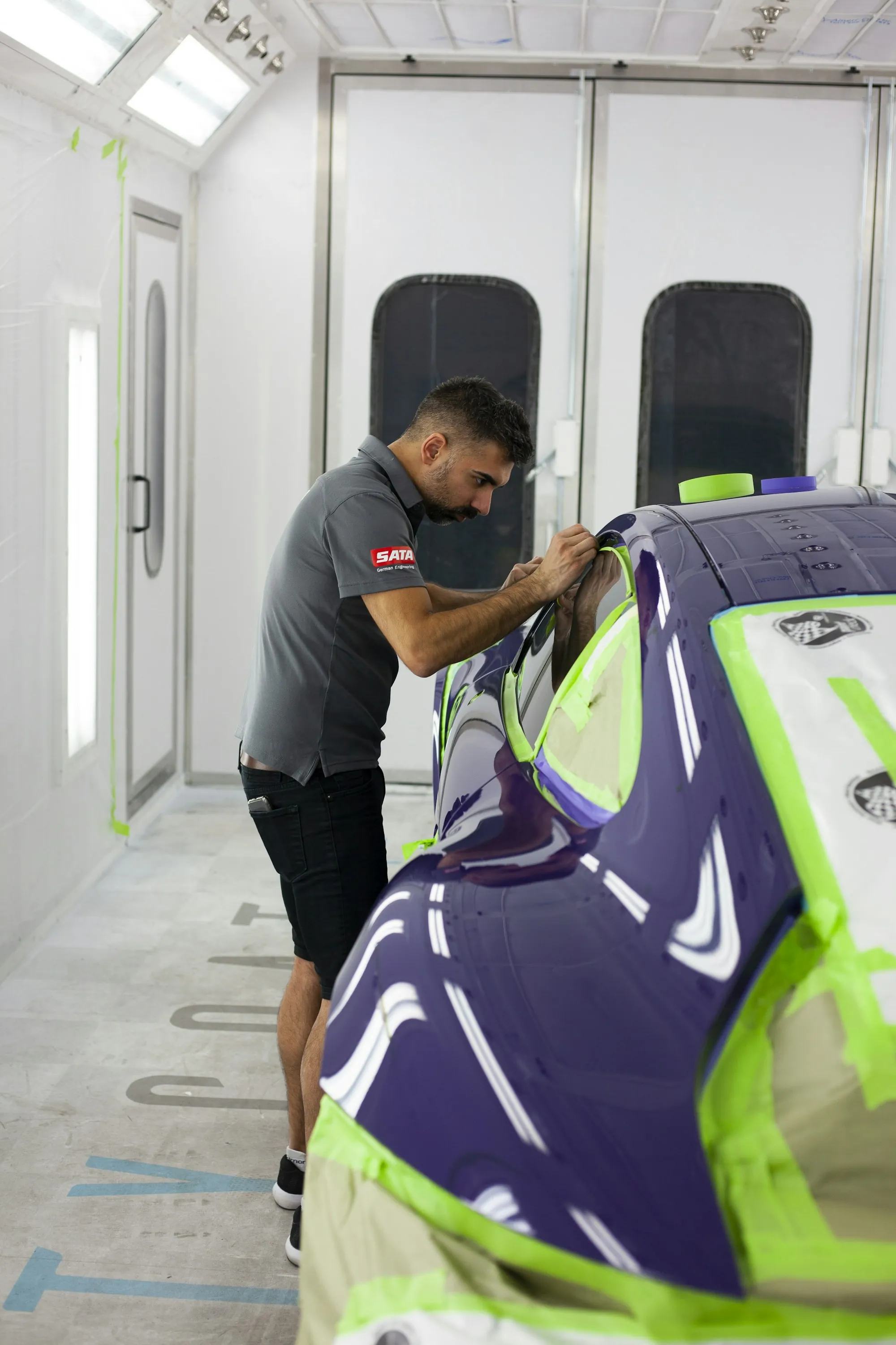 Technician applying film to a car inside a white spray booth